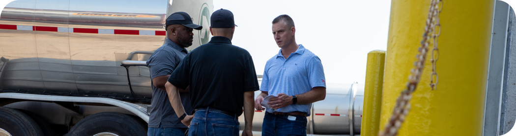 Three men outside by semi-trucks having a conversation